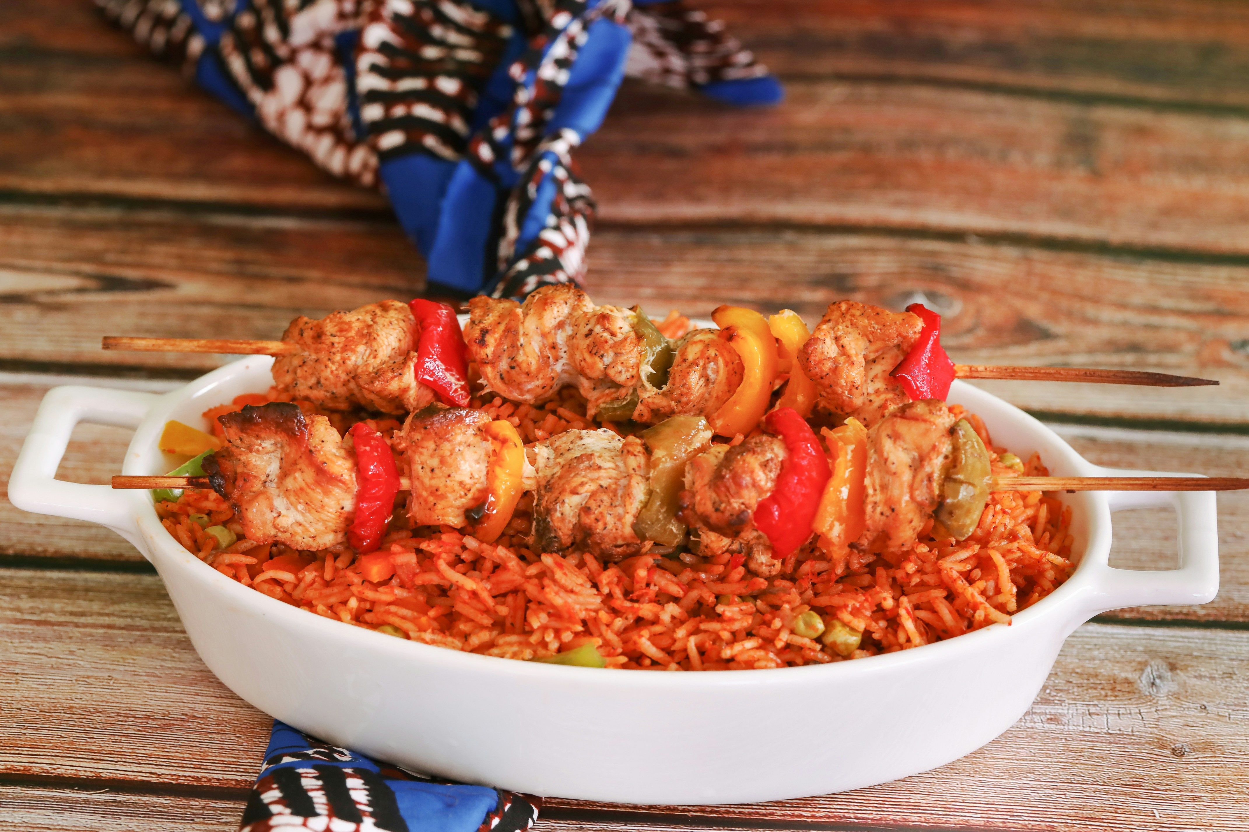 Jollof rice with chicken skewers served on a tray. 
