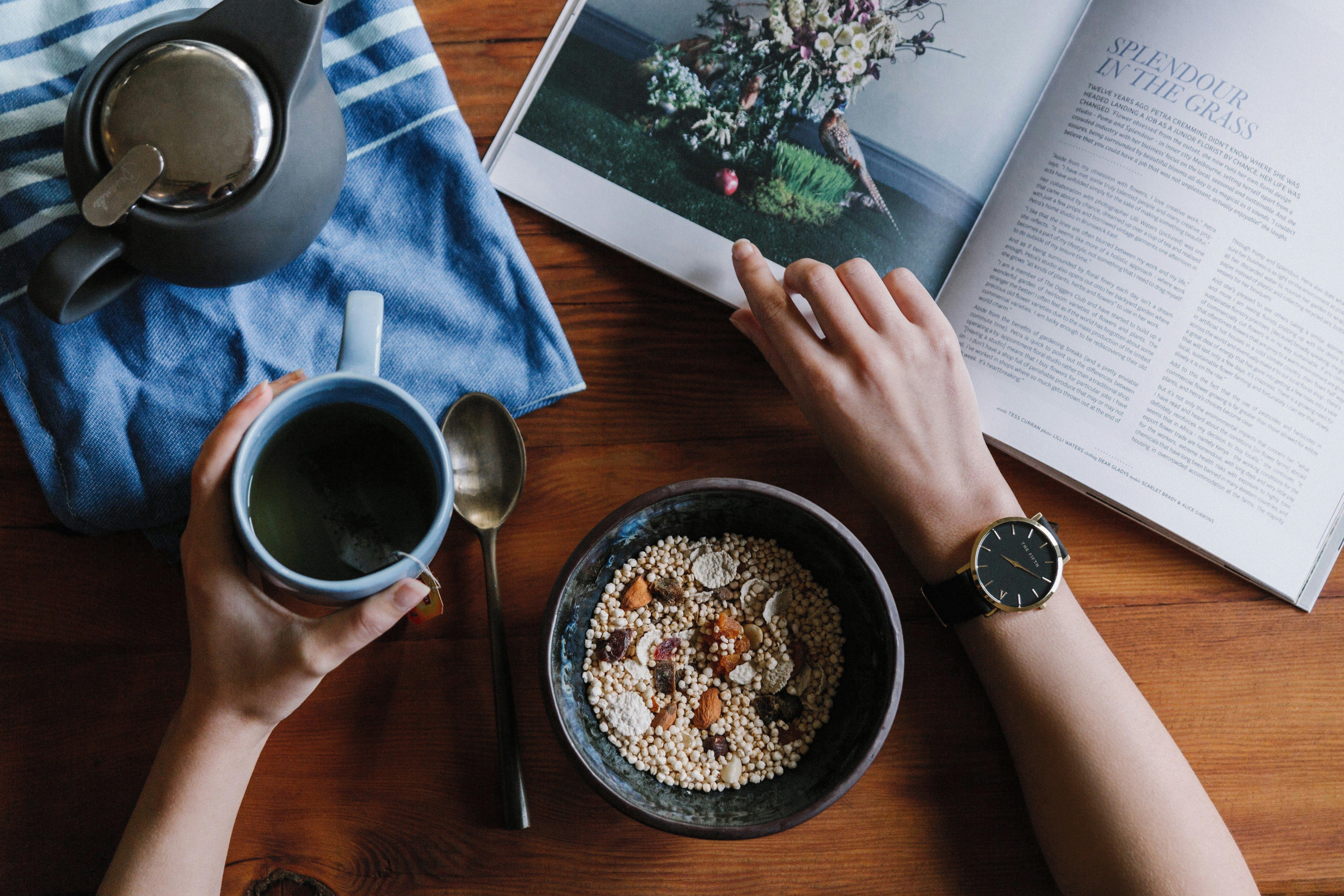 A bowl of quinoa with some dry fruits placed on a table as a person works on the table while eating from the bowl and sipping his drink from a mug.