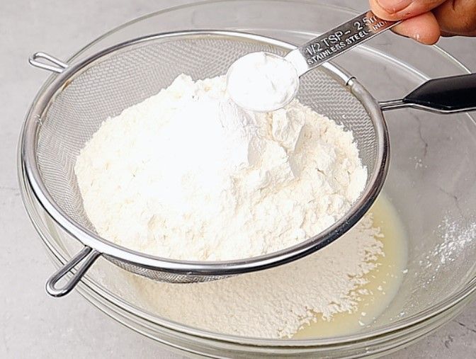 Step 1.4: Place a sieve over the bowl and add all-purpose flour, baking powder, baking soda, and salt