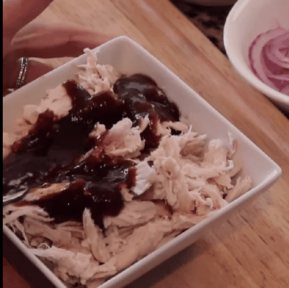Step 1.2: Spread BBQ sauce over the par-baked dough, then layer with mozzarella cheese, shredded chicken, red onions, and red bell peppers