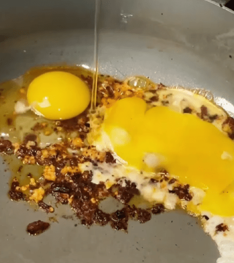 Step 1.1: In the same pan, add chili oil and crack in the eggs