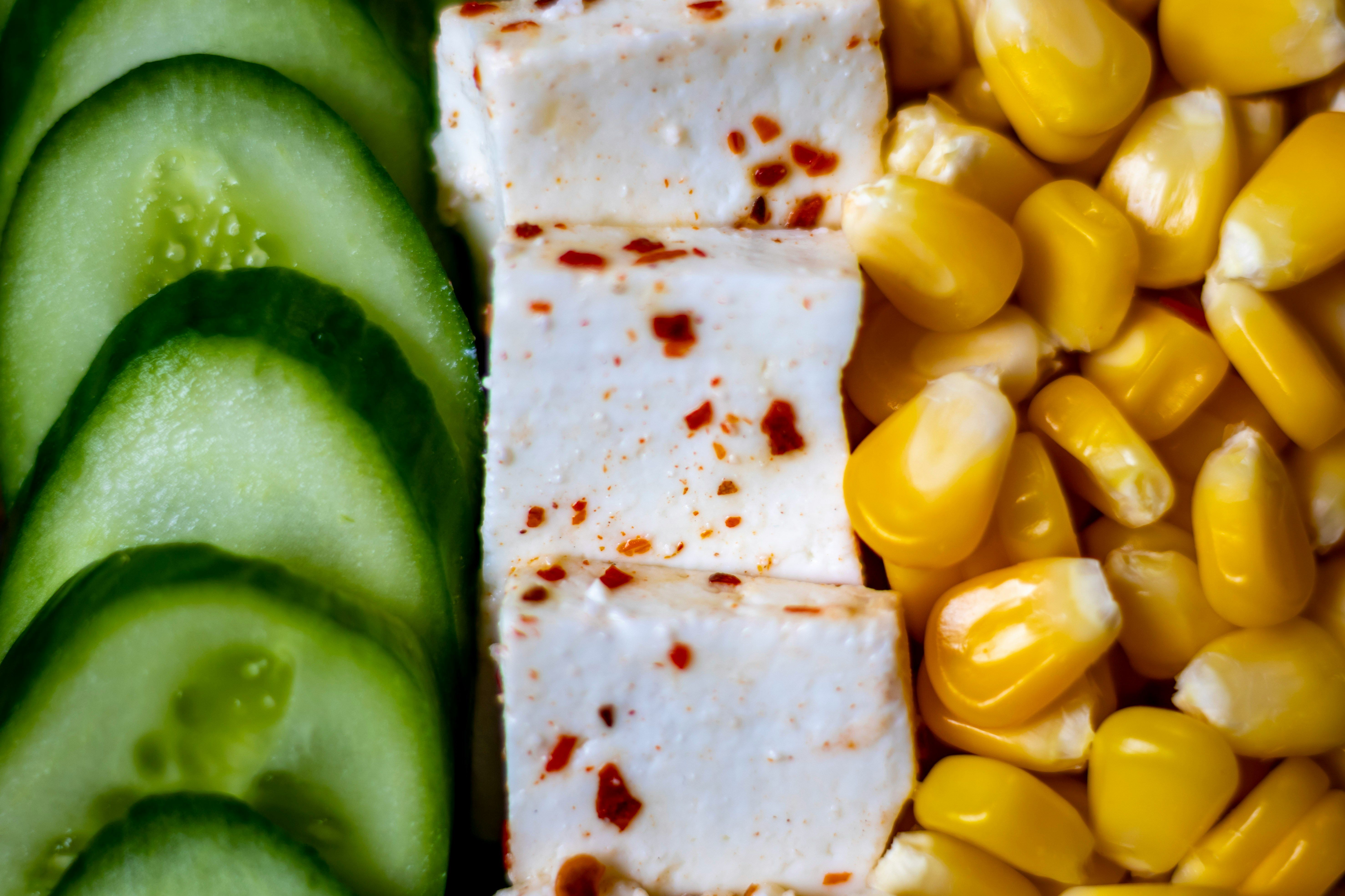 Tofu placed in a straight row with corn and cucumbers on both sides. 