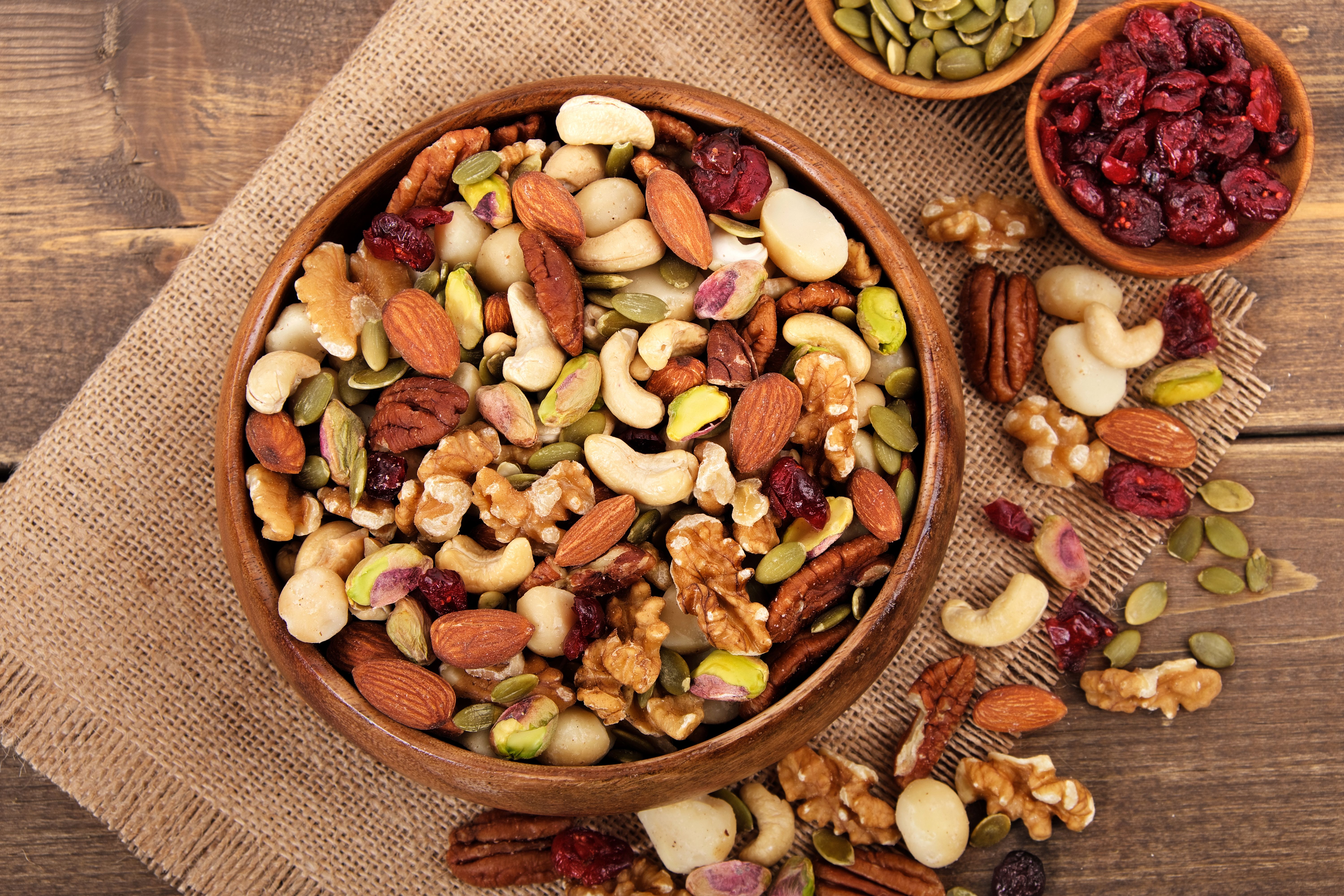 Assorted mixed nuts in a wooden bowl with pumpkin seeds, almonds, walnuts, and dried cranberries