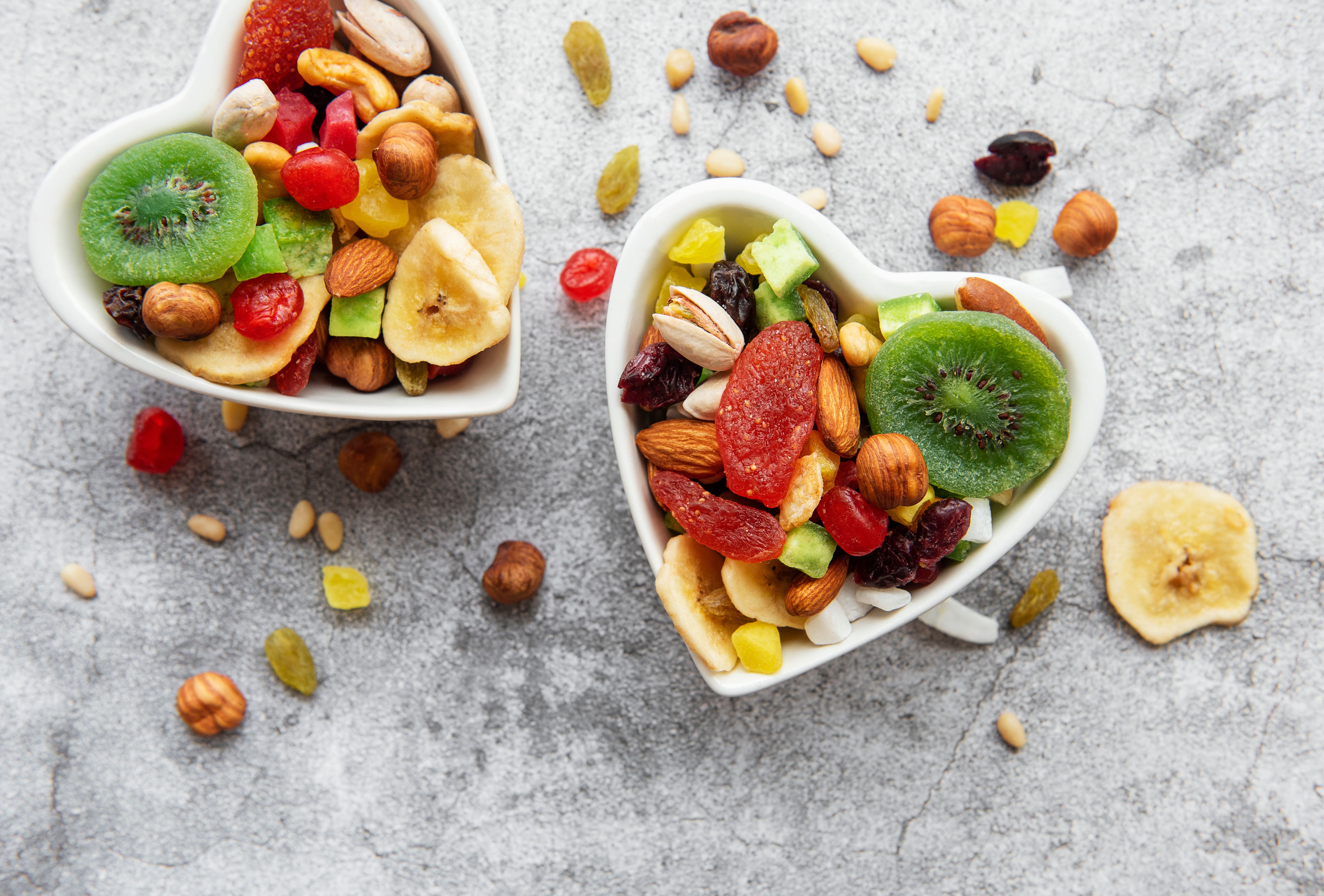 Assorted bowls of dried fruits and nuts on a gray concrete surface, perfect for healthy snacking.