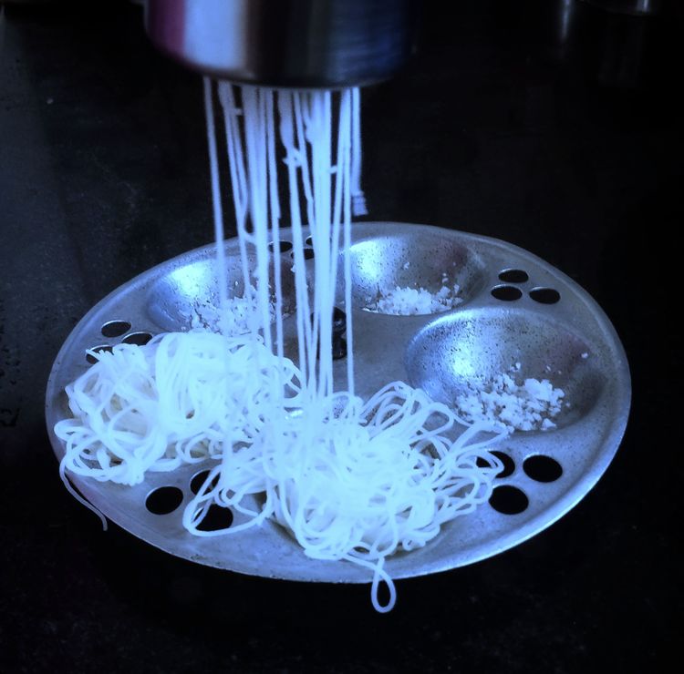 Step 1.1: Grease the steamer plate, spread some grated coconut, then press the dough through the idiyappam presser onto the steamer plate