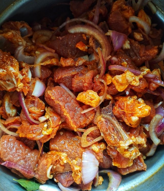 Step 1.1: In a bowl, combine the cleaned beef pieces with sliced onion, chopped garlic, chopped green chilli, chilli powder, turmeric powder, salt, coconut oil, and curry leaves