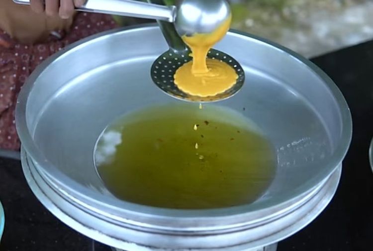 Step 2.1: Take a perforated ladle, place it on the hot oil, pour the batter over the ladle, and gently spread it using a spoon so that it drops into the hot oil