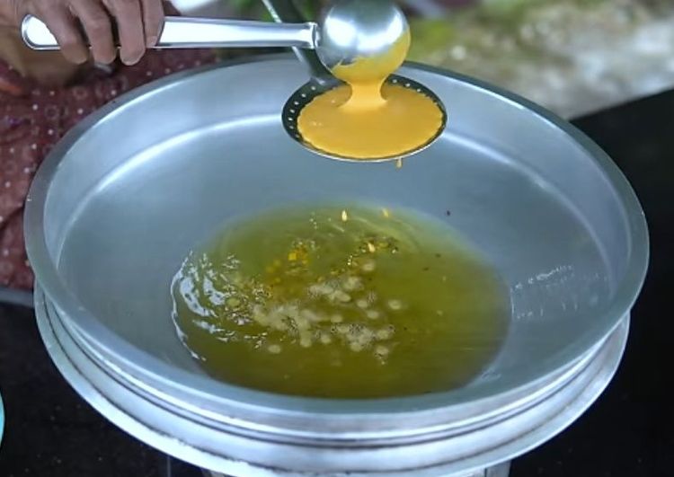 Step 2.2: Take a perforated ladle, place it on the hot oil, pour the batter over the ladle, and gently spread it using a spoon so that it drops into the hot oil
