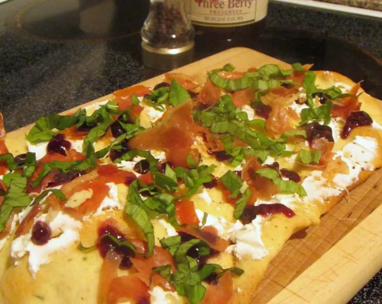Step 3.1: Once the flatbread is baked, spread the goat cheese and sprinkle crumbled prosciutto and ribbons of fresh basil leaves on top of the cheese