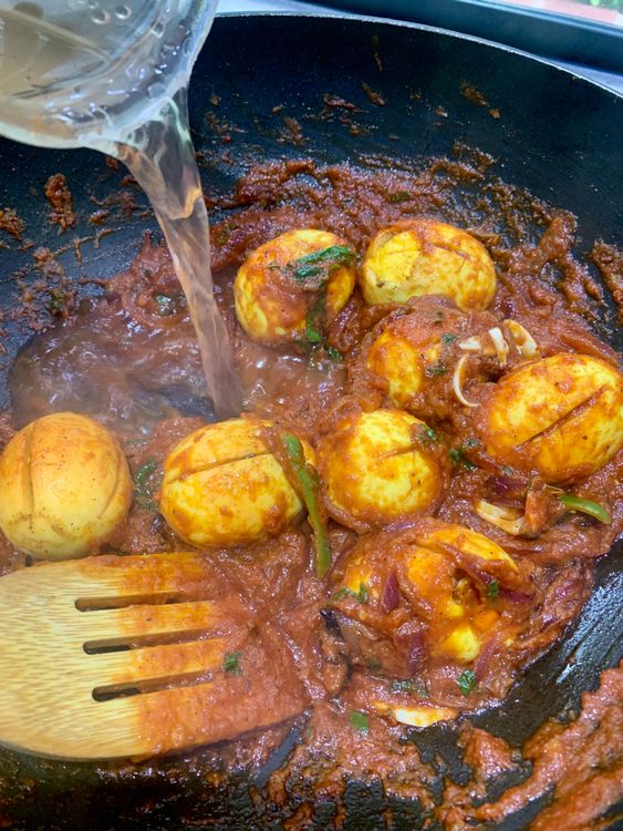 Step 3.1: Add the sautéed eggs, pour in water, stir, and cook until the masala thickens and looks glossy