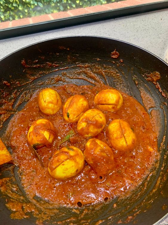 Step 3.2: Add the sautéed eggs, pour in water, stir, and cook until the masala thickens and looks glossy
