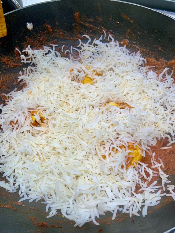 Step 4.1: Spread half of the rice evenly over the masala in the pot