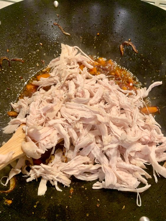 Step 2.1: Add the shredded chicken to the wok, stirring and cooking for a few minutes