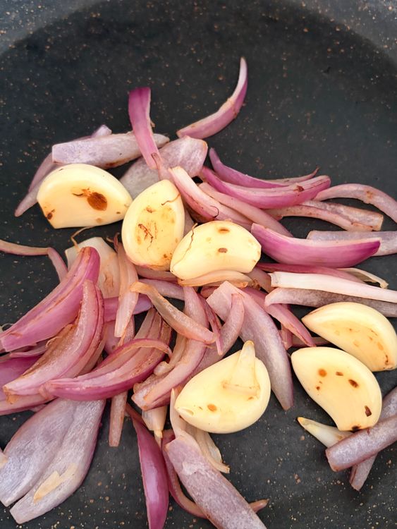 Step 1.1: In the same pan, dry roast the garlic cloves and sliced onion until lightly browned at the edges