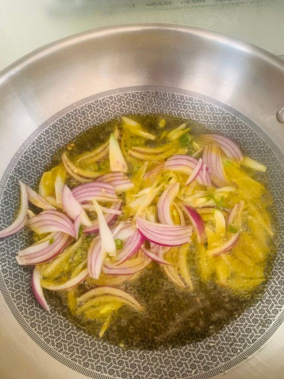 Step 1.1: Add the sliced onions and green chillies, stir-frying until the onion edges turn brown