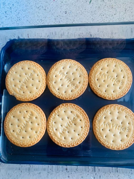 Step 3.2: Dip each Marie biscuit briefly into the milk and arrange them in a single layer at the bottom of a flat serving dish or glass container