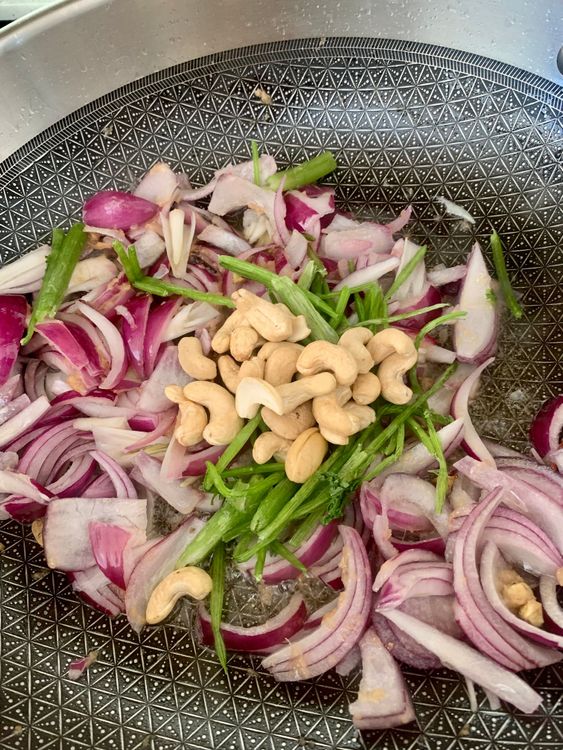 Step 4.1: Add sliced onions, coriander stems with leaves, green chillies, and cashews; sauté for 2–3 minutes until onions soften
