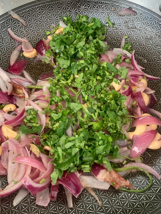 Step 4.2: Add sliced onions, coriander stems with leaves, green chillies, and cashews; sauté for 2–3 minutes until onions soften