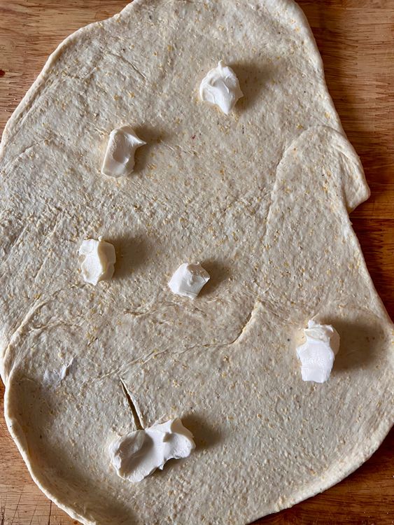Step 1.1: Taking a spatula, butter knife, or an icing tool, take half of the softened butter and spread all over the dough