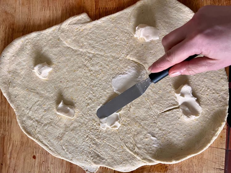 Step 1.2: Taking a spatula, butter knife, or an icing tool, take half of the softened butter and spread all over the dough