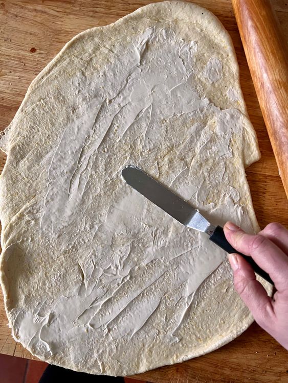 Step 1.3: Taking a spatula, butter knife, or an icing tool, take half of the softened butter and spread all over the dough