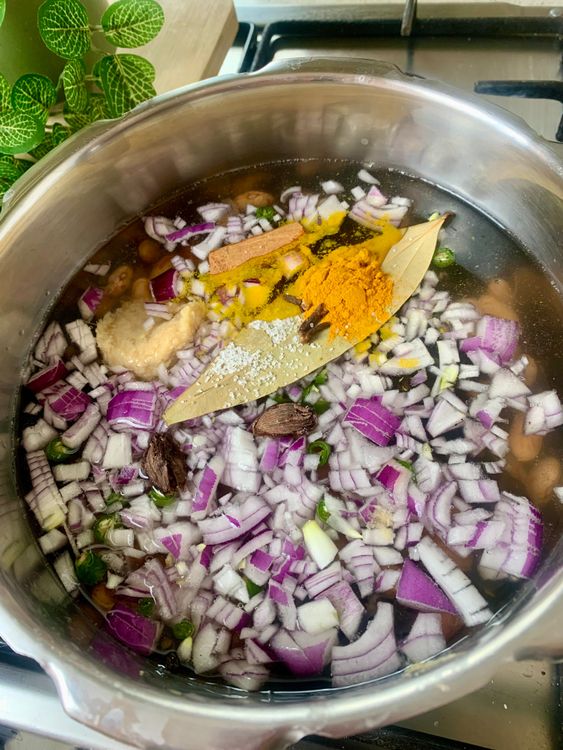 Step 1.1: Add soaked dal and rajma to a pressure cooker along with water, onion, green chilli, bay leaf, cinnamon, black cardamoms, cloves, ginger-garlic paste, salt, and turmeric