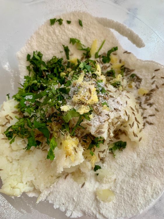 Step 2.1: In a large mixing bowl, add sabudana powder, grated boiled potatoes, ginger, green chilli, chopped coriander, cumin seeds, and salt/sendha namak