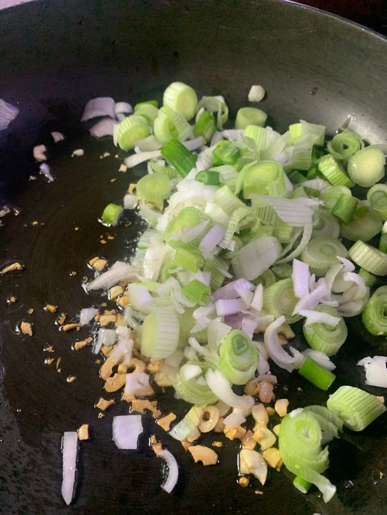 Step 2.1: After sautéing the garlic in oil, add the chopped spring onion, capsicum, and chopped green chillies to the pan