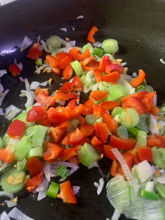 Step 2.2: After sautéing the garlic in oil, add the chopped spring onion, capsicum, and chopped green chillies to the pan