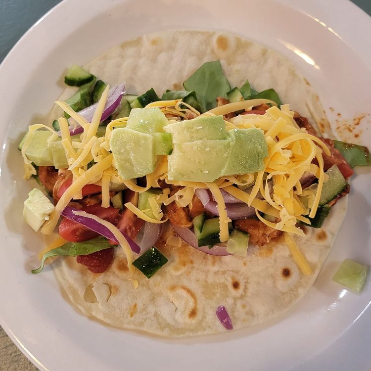 Step 2.2: Now build your tacos, starting with lettuce in the center, topped with chicken, tomatoes, cucumber, red onions, cheddar cheese, and avocado