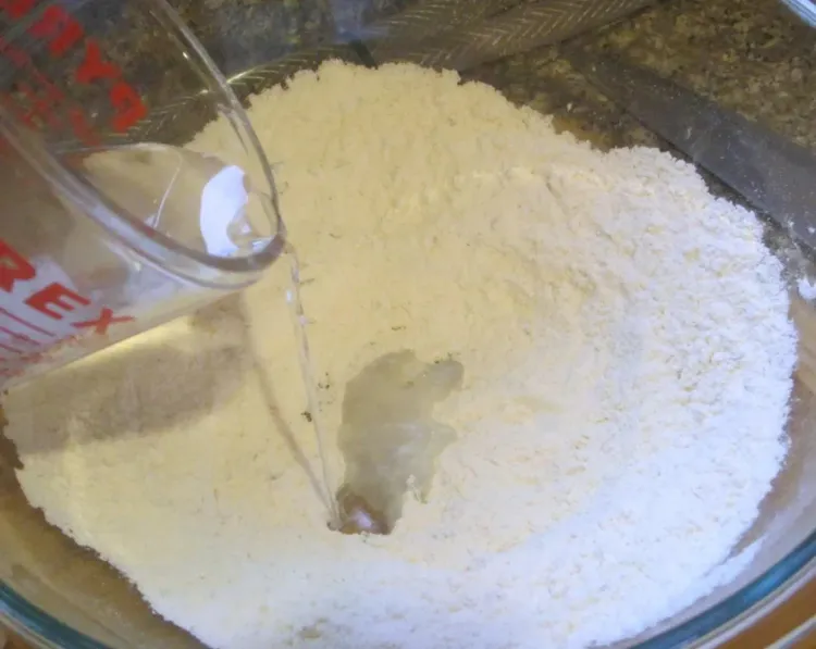 Step 2.1: Make a well in the center, then add water and olive oil and gradually stir into flour with a wooden spoon until a dough forms