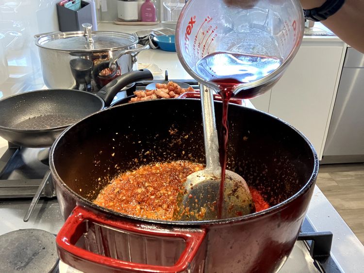 Step 2.2: Add the flour, mixing it through to coat everything, and then pour in the red wine to deglaze the base of the pan