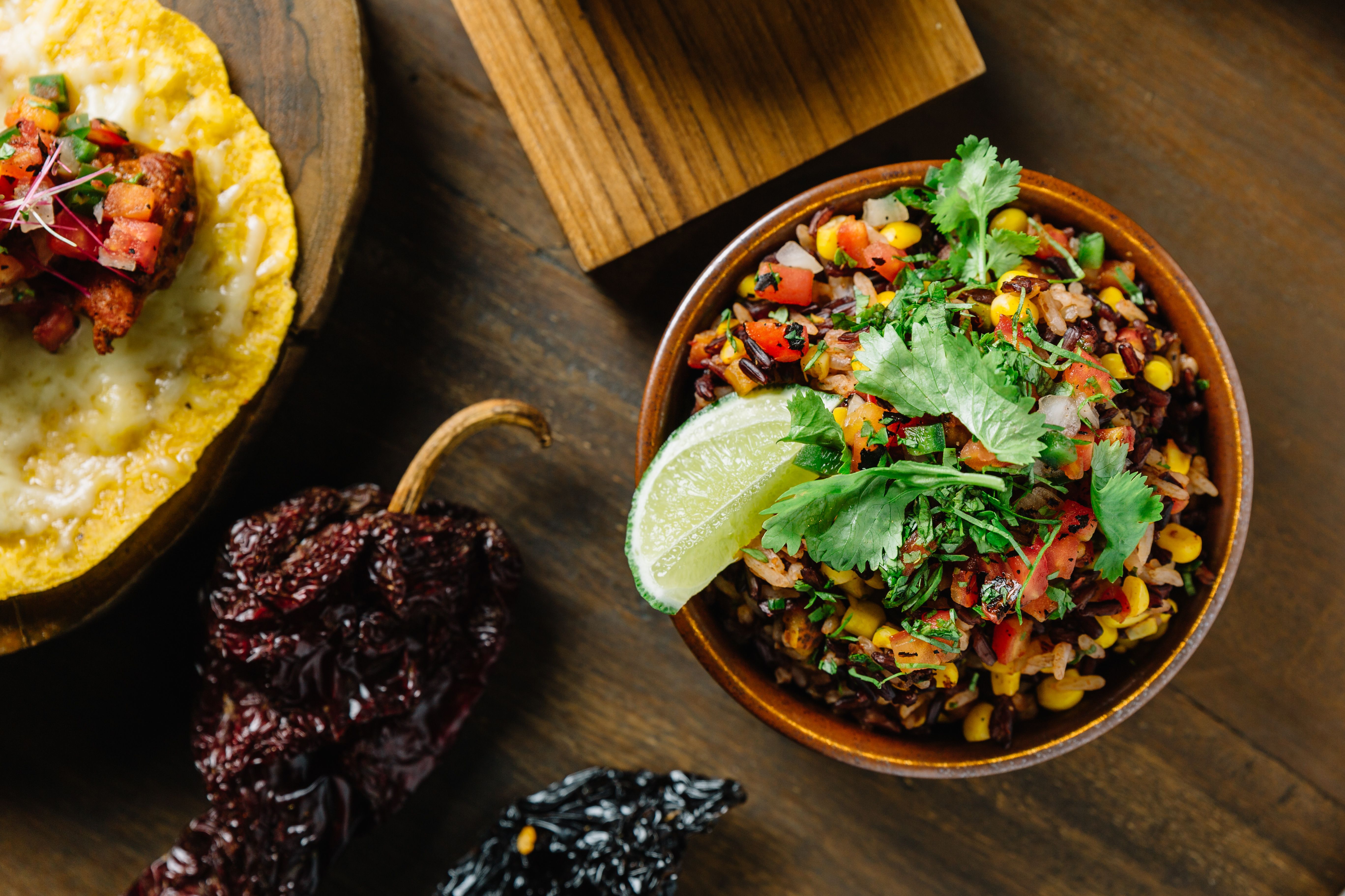 Colorful Mexican cuisine bowl featuring rice, salsa, corn, and lime with fresh cilantro garnish.
